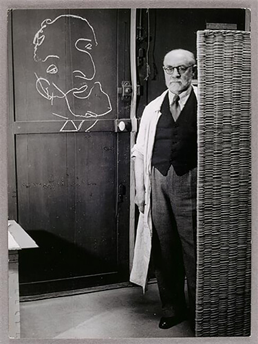 Henri Matisse standing against a screen and drawing with chalk, 1939<p>Courtesy Vintage Works, Ltd / © George Brassaï</p>