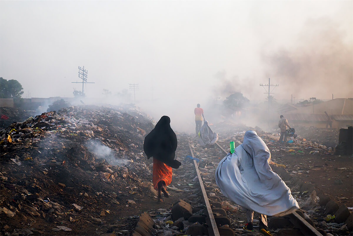 Locals go about their routines, stepping over garbage heaps that burn along the railroad tracks in Kaduna, Nigeria on April 3, 2013.<p>Courtesy VII Photo Agency / © Ed Kashi</p>