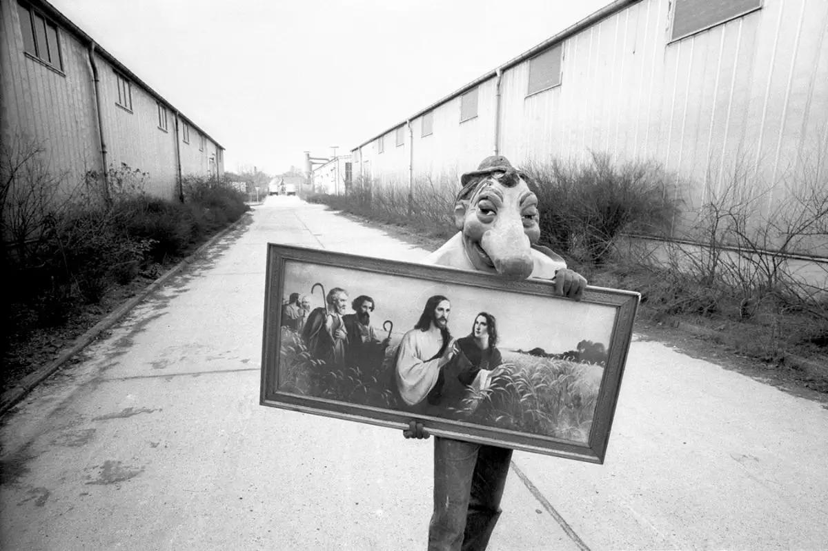 black and white photograph of masked person carrying a painting with Jesus leading modern people in Ireland