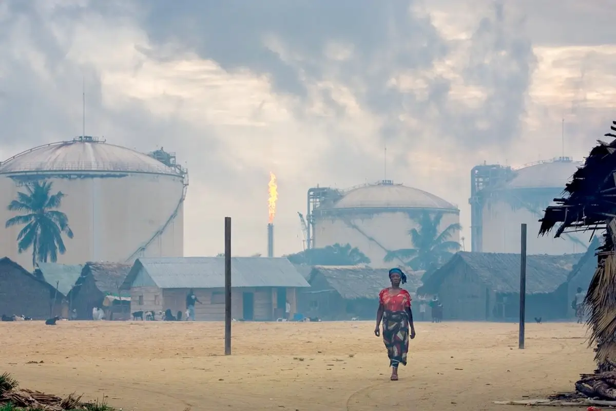color photograph of a woman walking with flaring gas burning behind her in the Niger Delta