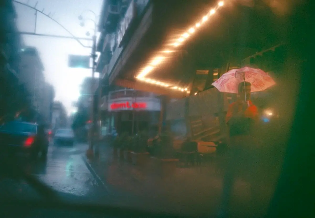 color photograph of a man walking through the rain with reflections on store windows on Hamra street, Beirut, Lebanon