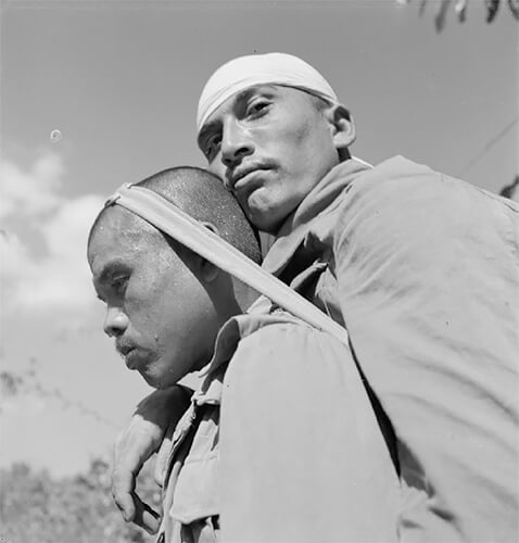 India 1944: A Gurkha soldier transporting a wounded man on his back through the jungle. © IWM Non Commercial Licence<p>© Cecil Beaton</p>