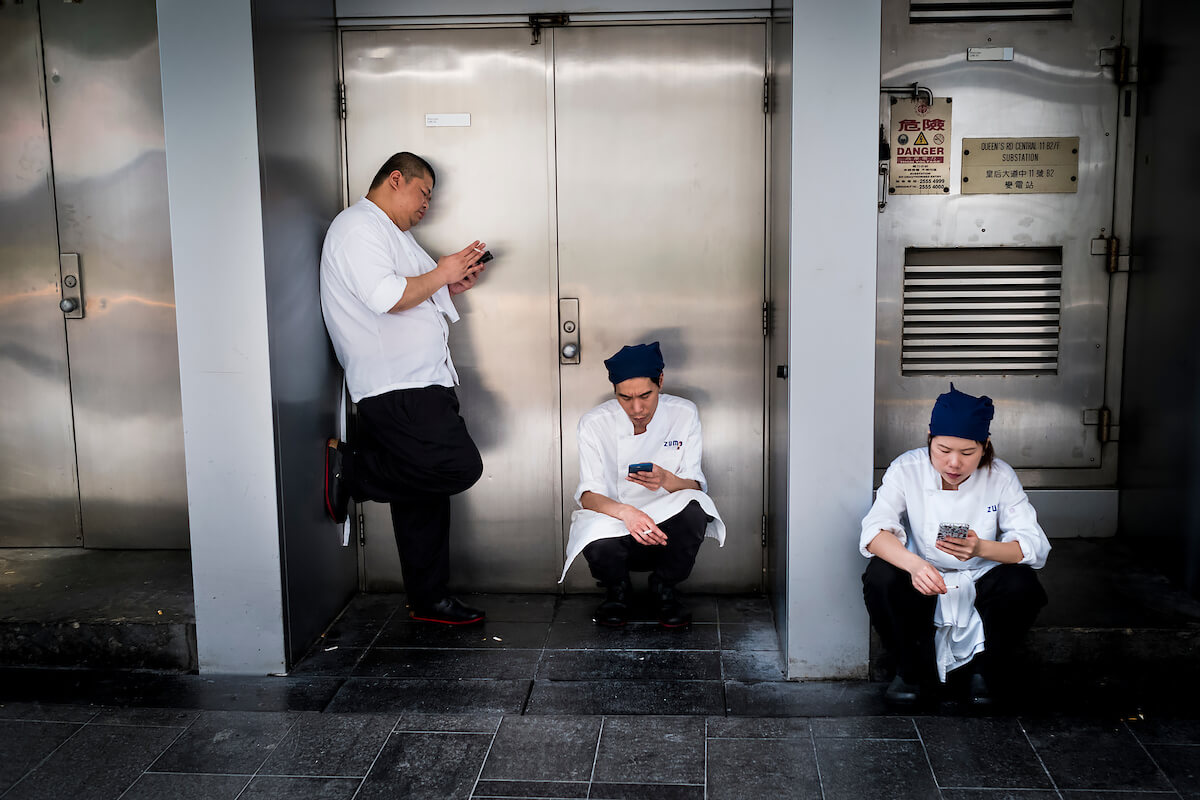 Men and woman smokes and checks their mobile phone on a street in Hong Kong during a work break on April 30, 2018<p>Courtesy Redux Pictures / © Jean-Michel Clajot</p>