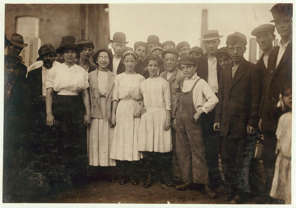 Group of workers, including boys and girls, standing outdoors. Lewis Hine