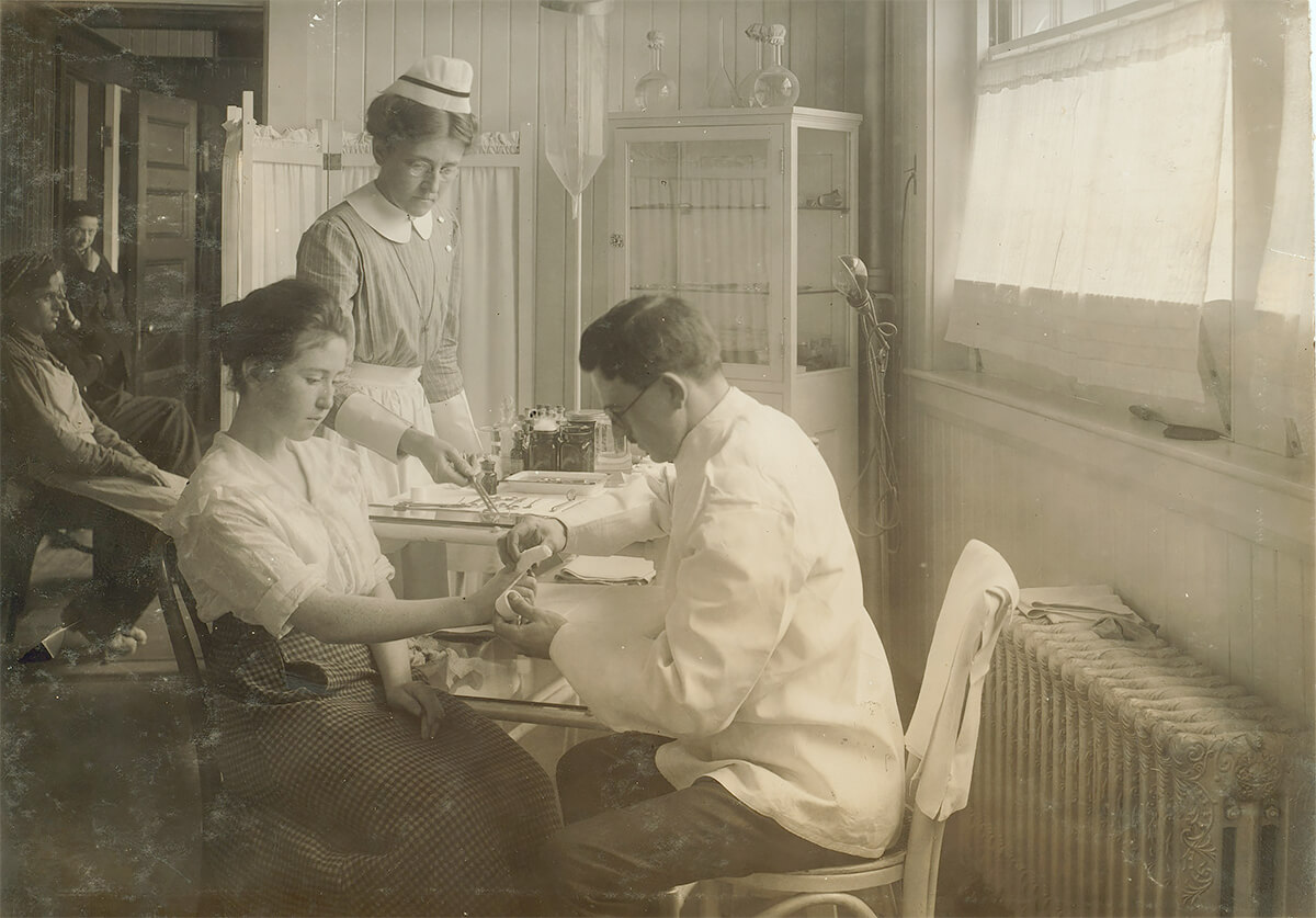 Woman with injured finger being administered first aid in the infirmary of the Hood Rubber Co., Cambridge, Massachusetts 1917 © Library of Congress <p>© Lewis Hine</p>