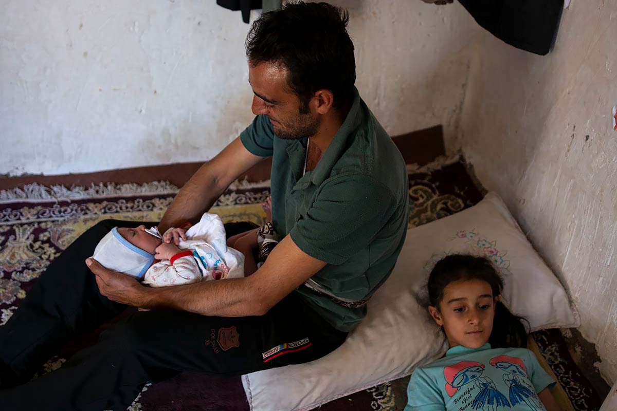 Kasra is in his father’s arms. Mahsa is watching TV. Among the Lurs people, taking care of children is the mother’s duty. Iran, September 2020.<p>© Sajedeh Zarei</p>