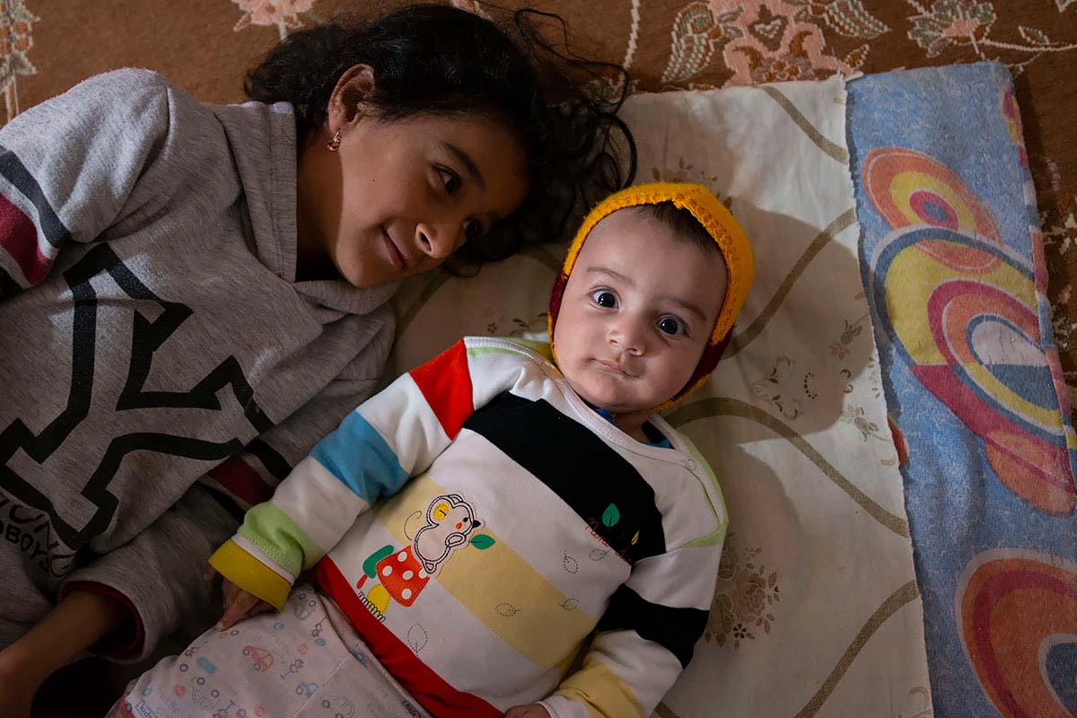 Mahsa is playing with Kasra. Kasra stares at the camera. Mahsa feels responsible for her brother and helps her mother. Amir Ayyub, Iran, January 2021.<p>© Sajedeh Zarei</p>